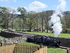 A steam train on the railway with a stone wall and trees in the background at Dakota near Boot