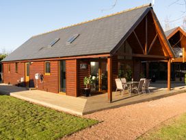 A wooden cabin with a sloped roof and an outdoor dining table on a wooden deck at The Green Monkey in North Hykeham