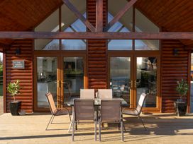 A wooden deck with a glass table and six chairs outside a cabin with glass doors at The Green Monkey in North Hykeham