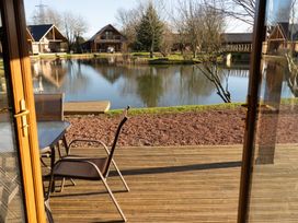 A wooden deck with chairs and table overlooking a pond with wooden houses around at The Green Monkey in North Hykeham
