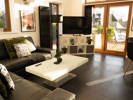 A living room with black leather sofas a white coffee table a TV on a shelf and glass doors at The Green Monkey in North Hykeham