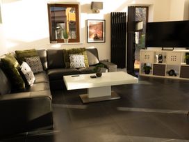 A living room with a black leather sectional sofa green and patterned pillows a white coffee table a black floor lamp and a television on a white stand at The Green Monkey in North Hykeham