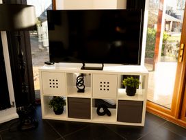 A television on a white entertainment unit with plants and decorative items next to a floor lamp and glass door at The Green Monkey in North Hykeham