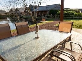 A glass outdoor table with a metal candle holder and several chairs on a wooden deck near a pond at The Green Monkey in North Hykeham