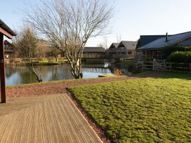A lake with trees and wooden cabins surrounding it with a wooden deck and grassy area at The Green Monkey in North Hykeham