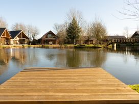 A wooden dock overlooking a pond with wooden cabins and a footbridge at The Green Monkey in North Hykeham