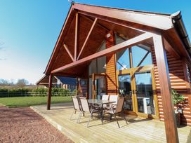 A wooden cabin with glass doors and an outdoor dining table with chairs on a deck at The Green Monkey in North Hykeham