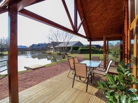 A covered wooden deck with a table and six chairs overlooking a pond and wooden houses at The Green Monkey in North Hykeham