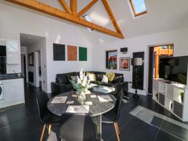 An open living and dining area with a round table and black chairs a black leather sectional sofa and a TV on a white stand at The Green Monkey in North Hykeham