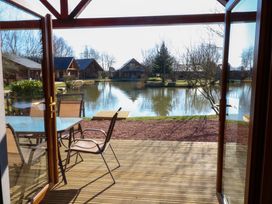 A patio with table and chairs overlooking a lake with cabins and trees at The Green Monkey in North Hykeham