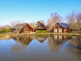 Three wooden cabins near a pond with trees in the background at The Green Monkey in North Hykeham