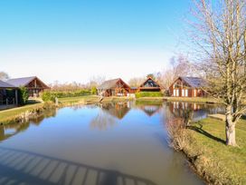 A pond with wooden houses and trees around it at The Green Monkey in North Hykeham