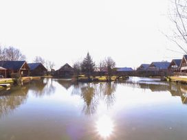 A pond with trees and wooden houses around it at The Green Monkey in North Hykeham