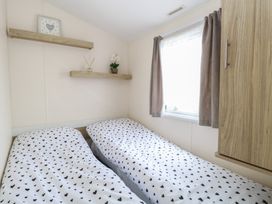 A bedroom with two beds with heart patterned bedding a window with curtains and wooden shelves at 31B Foxburrow Hang in Fritton near Belton Norfolk