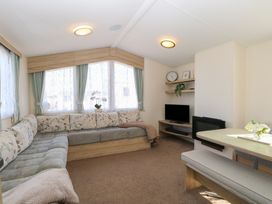 A living room with an L-shaped sofa, a TV on a wooden stand, shelves with decorations, and a dining table with a bench at 31B Foxburrow Hang in Fritton near Belton Norfolk