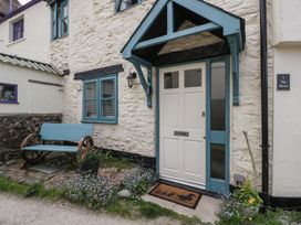 A white door with blue trim and a porch canopy beside a window and a blue bench outside with plants at 1 The Mews in Porlock