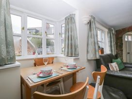 A dining table set for two with bowls and glasses next to windows with curtains and a black leather couch with cushions in a living area at 1 The Mews in Porlock