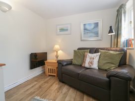 A small living room with a brown leather sofa with three cushions by a wooden side table with a lamp and two framed pictures on the wall at 1 The Mews in Porlock