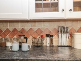 A kitchen countertop with two mugs a French press jars a wire chicken shaped basket salt and pepper shakers a set of knives and a container at 1 The Mews in Porlock
