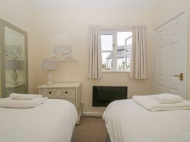 A bedroom with two single beds with folded towels a bedside table with a lamp a wall mirror a window with curtains and a white door at 1 The Mews in Porlock