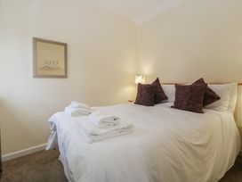 A bedroom with a bed with white sheets and brown pillows next to a lamp and a mirror on the wall at 1 The Mews in Porlock