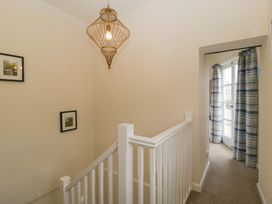 A carpeted stairway with white railing leading to a hallway with a window covered by blue striped curtains at 1 The Mews in Porlock
