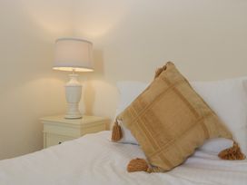A bedside table with a lamp next to a bed with white sheets and a brown cushion at 1 The Mews in Porlock