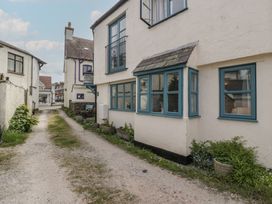 A narrow gravel path alongside white houses with blue window frames and small plants at 1 The Mews in Porlock