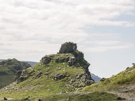 A rocky hill covered in grass with a trail and people walking on it in a mountainous area