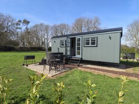A green metal shepherd hut with a small outdoor seating area and a barbecue on grass in a rural setting at Buttercup in Ashby-cum-Fenby near Waltham