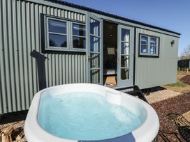 An outdoor hot tub in front of a corrugated metal cabin with open double doors at Buttercup in Ashby-cum-Fenby near Waltham