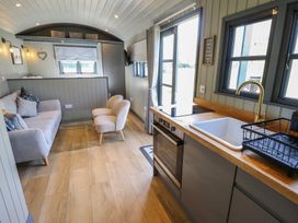 A kitchen with a sink oven and stovetop next to a living area with a sofa two chairs and a glass coffee table at Buttercup in Ashby-cum-Fenby near Waltham