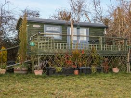 A small raised wooden cabin with a porch surrounded by potted plants and trees at Perch Hut in Hadlow Down near Crowborough