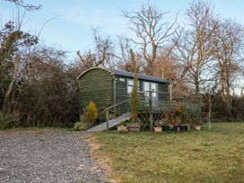 A small green wooden hut on stilts with a ramp and potted plants around it in a grassy area with leafless trees at Perch Hut in Hadlow Down near Crowborough