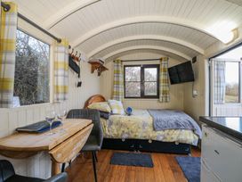 A small room with a bed a wall-mounted television a wooden table with two chairs and windows with yellow plaid curtains at Perch Hut Hadlow Down near Crowborough