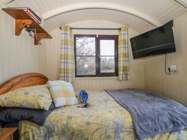 A small bedroom with a bed under a window with plaid curtains a mounted television and a wooden shelf on the wall at Perch Hut Hadlow Down near Crowborough