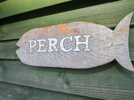 A wooden fish-shaped sign with the word PERCH on a green wooden wall at Perch Hut Hadlow Down near Crowborough