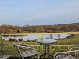 An outdoor seating area with a round glass table and two wicker chairs overlooking a pond and fields at Perch Hut in Hadlow Down near Crowborough