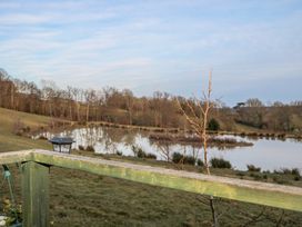 A wooden railing overlooking a pond with trees and grassland in the background at Perch Hut in Hadlow Down near Crowborough