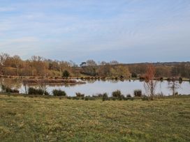 A pond surrounded by grass and trees under a cloudy sky at Perch Hut in Hadlow Down near Crowborough