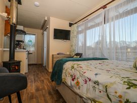 A bedroom with floral bedding a small stove a wall-mounted television and a large window with sheers at Tench Hut in Hadlow Down near Crowborough