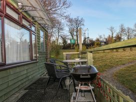 Outdoor patio with chairs table and barbecue grill next to a green wooden building at Tench Hut in Hadlow Down near Crowborough