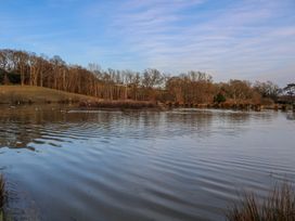 A lake with ripples and trees around it under a blue sky at Tench Hut in Hadlow Down near Crowborough