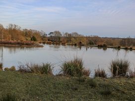 A pond surrounded by grass and trees with two people standing near the water at Tench Hut in Hadlow Down near Crowborough