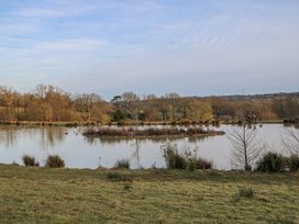 A small lake with an island in the center surrounded by grass and trees at Tench Hut in Hadlow Down near Crowborough