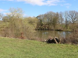 An outdoor scene with grass in the foreground trees and a pond in the background at Tench Hut Hadlow Down near Crowborough