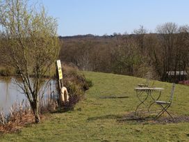 A grassy area with a table and two chairs near a pond with a tree and a safety sign at Tench Hut in Hadlow Down near Crowborough