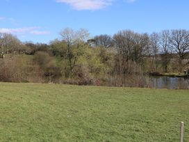 A grassy field with leafless trees and a pond under a clear sky at Tench Hut in Hadlow Down near Crowborough