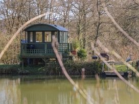 A small cabin on stilts next to a pond with a wooden dock and trees in the background at Roach Hut in Hadlow Down near Crowborough