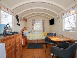 An interior of a small cabin with a bed at the end a wooden cabinet with a kettle a dining table with two chairs and windows on both sides at Roach Hut Hadlow Down near Crowborough